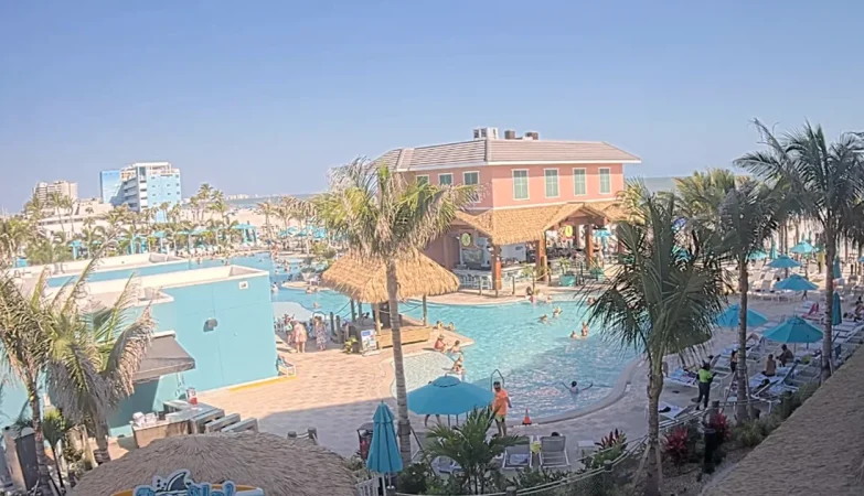View of the vibrant Margaritaville Fort Myers Beach resort, featuring a sparkling pool surrounded by palm trees and loungers, as seen from the Fins Up Beach Club.